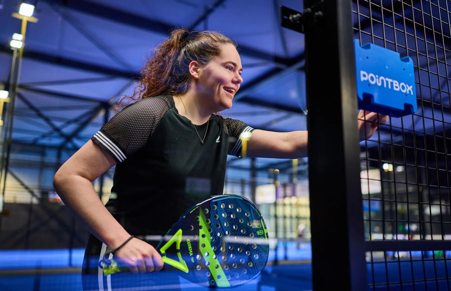 Padelspeelster start lachend haar wedstrijd op het Pointbox touchscreen naast de baan